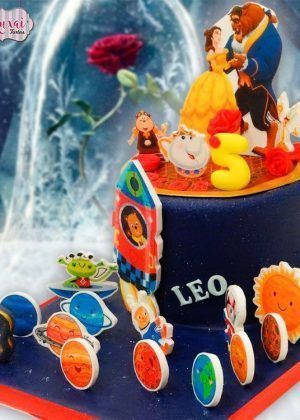 Tarta Bella y Bestia y el osito Tito con figuras de Bella, la Bestia, la Tetera y planetas sonrientes alrededor de la base