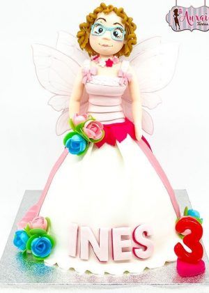 Tarta hada tipo Princesa con figura grande de hada con alas transparentes, cabello rizado, gafas azules y vestido blanco, nombre INES y número 3