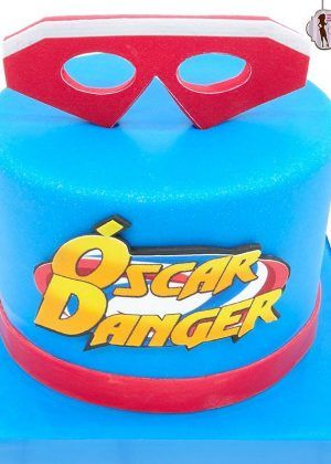 Tarta máscara Henry Danger en azul con máscara roja grande en la parte superior y logo ÓSCAR DANGER en la parte frontal