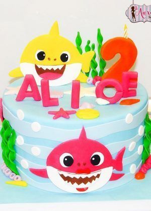 Tarta Baby Shark 2 en azul con Baby Shark amarillo, Mommy Shark rosa, número 2 naranja y nombre ALIOE en letras rosas