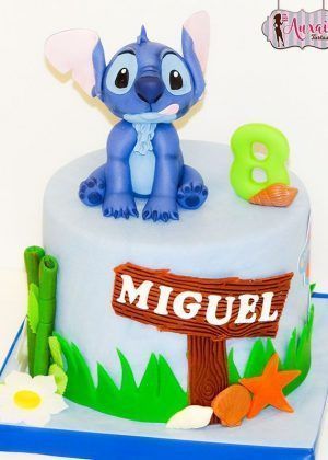 Tarta Disney Stitch en azul con figura grande de Stitch, cartel de madera con nombre MIGUEL, número 8 y decoración tropical
