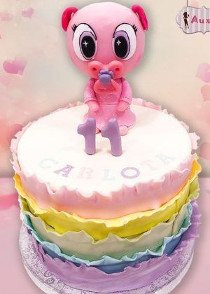 Tarta Ksi-meritos arco iris en tonos pastel con figura grande de Ksi Meritos, número 1 y nombre CARLOTA en la superficie