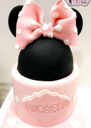 Tarta Disney media cabeza de Minnie Mouse con cabeza negra, orejas y gran lazo rosa con lunares sobre base rosa con nombre Micaela
