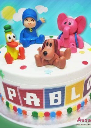 Tarta Pocoyo personalizada con figuras 3D de Pocoyo, Pato, Elly y Lou sobre superficie blanca y nombre Pablo en letras multicolores