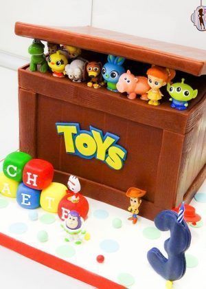 Tarta Disney Caja de juguetes Toy Story con baúl marrón abierto, personajes de Toy Story asomando, logo TOYS en amarillo, nombre NATE en cubos de colores y número 3 con vela
