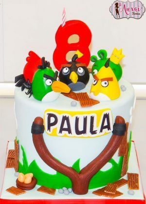 Tarta Angry Bird pequeña con pájaros rojo, negro y amarillo sobre troncos, número 8 rojo grande con vela y nombre PAULA en cartel frontal con honda marrón