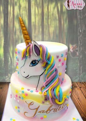 Tarta unicornio pintada a mano de dos pisos con cabeza de unicornio pintada a mano, melena en tonos rosa azul y amarillo, cuerno dorado y nombre GABRIELA en letra cursiva dorada