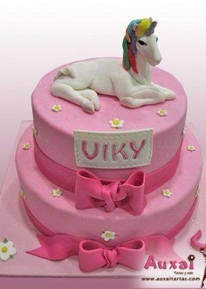 Tarta unicornio realista de dos pisos en rosa con figura 3D de unicornio tumbado con melena multicolor, lazos grandes y placa con nombre VIKY