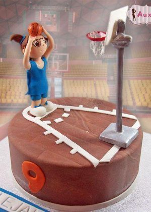 Tarta baloncesto niña personalizada con figura de jugadora en uniforme azul, canasta blanca y naranja, base marrón y acabados profesionales