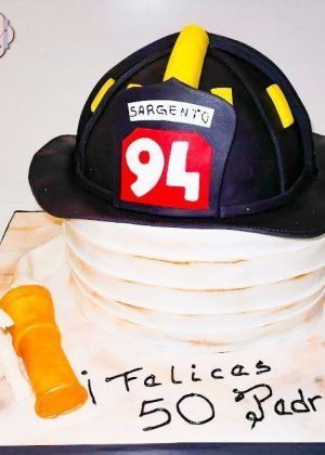 Tarta bombero con casco negro y número rojo, base blanca y crema, detalles amarillos