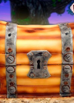 Tarta Personalizada Fortnite cofre con diseño de cofre del tesoro en fondant dorado sobre fondo de batalla en purpura y azul