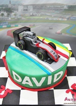 Tarta personalizada en forma de coche de Fórmula 1 con diseño en fondant rojo, blanco y verde. Incluye nombre personalizado y detalles del piloto. Postre motor profesional para celebraciones especiales.