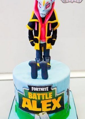 Tarta personalizada en forma de personaje Drift de Fortnite con fondant premium en tonos amarillo, rojo, azul y verde. Base decorada con logo FORTNITE BATTLE ROYALE.