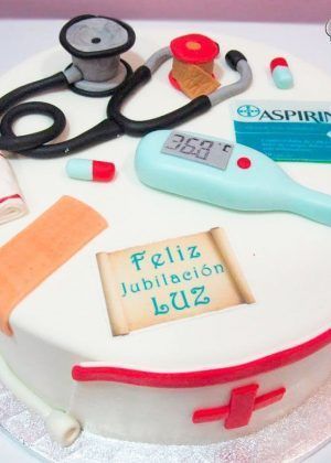 Tarta temtica enfermera médico con fondant blanco, cruz roja decorativa y papel naranja con símbolos médicos. Creación artesanal personalizada para homenajear a profesionales sanitarios.