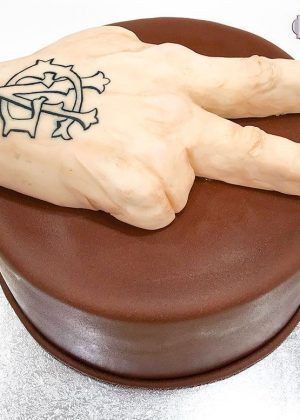 Tarta mano realista Gianluca Vacchi con tatuaje GV y gesto victoria sobre base chocolate – ideal para cumpleaños extravagantes