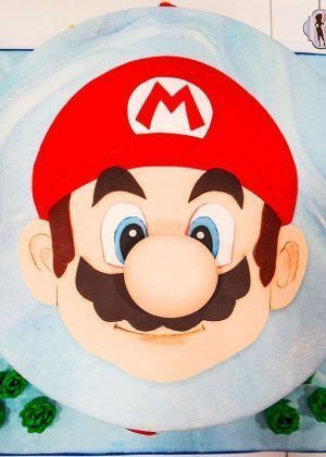 Tarta cara Super Mario en 2D con gorra roja, bigote y fondo azul cielo – ideal para cumpleaños de fans de Nintendo