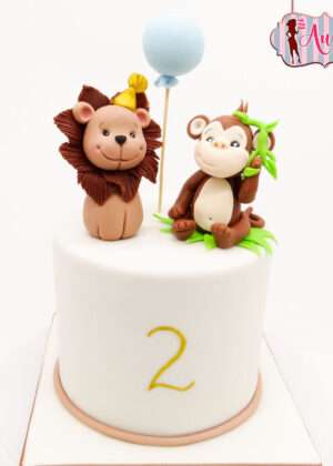 Tarta sencilla animales mono y león en Madrid con figuras de fondant y número dos dorado para cumpleaños infantil.