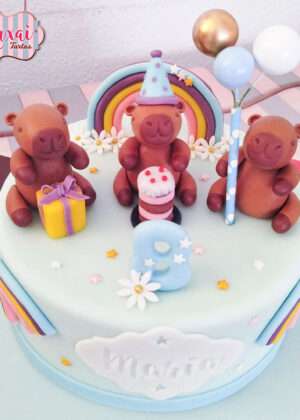 Tarta de cumpleaños personalizada madrid con figuras de fondant de capibaras, arcoíris y globos en tonos pastel