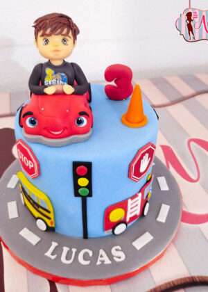 Tarta infantil coche animado en Madrid con figura de fondant de niño en coche rojo y señales de tráfico
