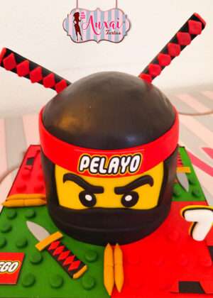 Tarta infantil lego 3d inspirada en un personaje ninja de color negro con katanas rojas sobre base de bloques verdes en Madrid