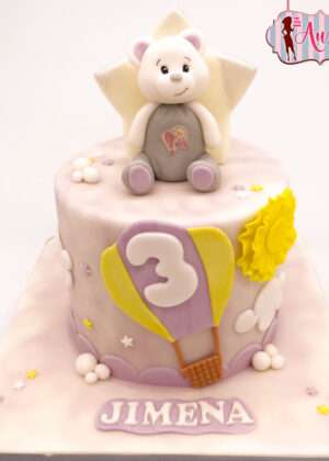 Tarta infantil osito de peluche con globo aerostático lila y sol amarillo, elaborada por Auxai Tartas en Madrid.