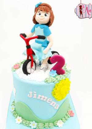 Tarta infantil personalizada madrid con figura modelada en 3D de niña en triciclo rojo y decoración campestre de sol y flores de Auxai Tartas.