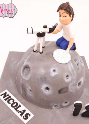 Tarta nino astronomo modelada en fondant con forma de luna gris con cráteres y telescopio en Madrid.