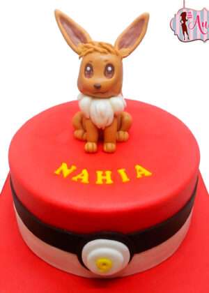 Tarta pokemon ibi con diseño de Pokéball roja y blanca y una adorable figura modelada a mano de Eevee con letras amarillas personalizadas.