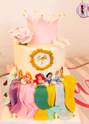 Tarta princesas Disney con corona modelada en rosa y oro sobre drapes de fondant de colores en Madrid
